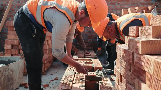Builders building a brick wall. Construction work on construction. The masters lay bricks and build the wall of the house.