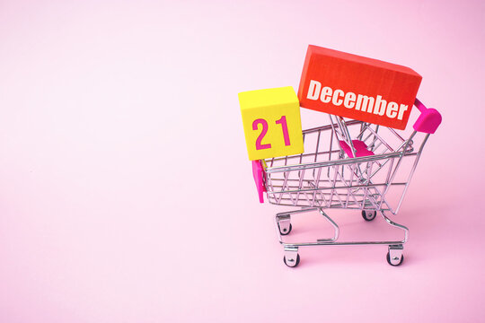 December 21st . Day 21 of month, Calendar date. Close up toy metal shopping cart with red and yellow box inside with Calendar date on pink background. Winter month, day of the year concept.