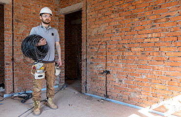 A worker at a construction site holds an electrical cable.