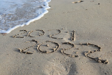 2021-2022 escrito en la arena con ola de fondo y huella