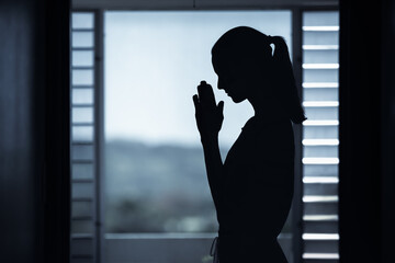 Female silhouette with praying hands indoors. 
