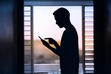 Silhouette of young male indoors holding smartphone	