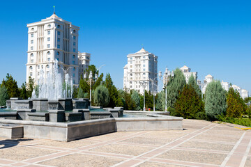 Square in Ashgabat, Turkmenistan showing water fountain and multiple newly-erected white marble residential buildings behind.