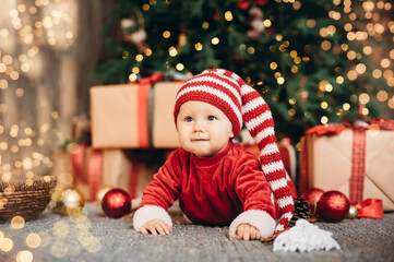 Little child under Christmas tree. baby girl in Santa Claus hat with gifts under Christmas tree