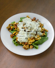 Green pappardelle pasta with tofu, beans and white vegan bechamel sauce with mushrooms in white dish. Homemade meal centered on clean wooden background