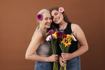 Two smiling women of different ages standing head to head in studio. Caucasian females with bouquets in hands and flowers in their hair.