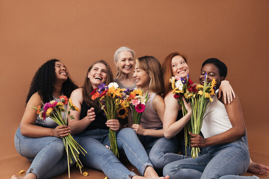 Group of multi-ethnic women sitting together in studio. Six smiling females with bouquets of flowers.