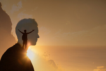 Silhouette of a man climbing to the top of a mountain with arms up to the sky. young man looking to...