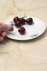 Hand picking delicious and healthy red cherries from a decorated white dish.