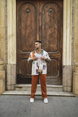 Hot caucasian man with arm tattoos with a patterned shirt and brown pants posing in the street