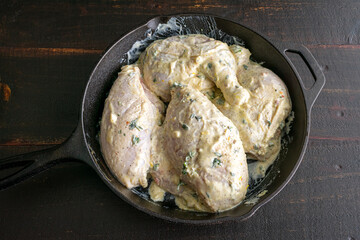 Marinated Chicken Quarters in a Cast-Iron Skillet: Uncooked chicken pieces marinated in Greek...
