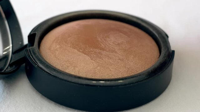 Big lush brush gains powder, bronzer and highlighter on pile to be used in make-up. Artist working with face palette. Details of working process, tools in beauty industry. Decorative cosmetics.