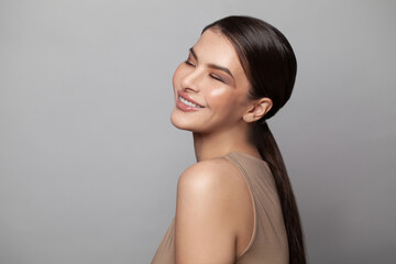 Pretty woman with closed eyes and dark eyebrows smiling on gray background. Attractive female model...