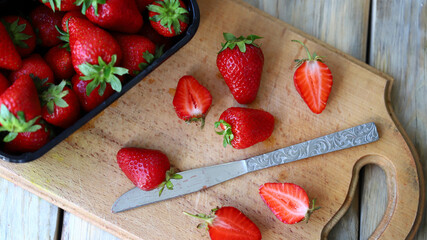 Strawberry slices on a wooden board. Knife. Tray with strawberries.