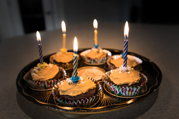 Birthday cupcakes with candles burning warm light glowing in the dark. Homemade baked cupcake platter celebration background