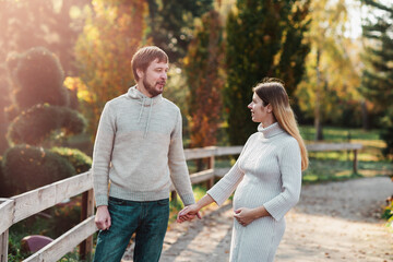 Obraz premium Family together in autumn park. Happy couple Husband and his pregnant wife relaxing in nature. happy married couple expecting baby. Pregnancy, maternity concept. Parents hands on pregnant belly