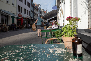 Fototapeta na wymiar Selective focus at outdoor rusty metal table, vase bottle with flower and chair without people in front of Cafe, bar, and restaurant on famous walking street in old town Düsseldorf, Germany.