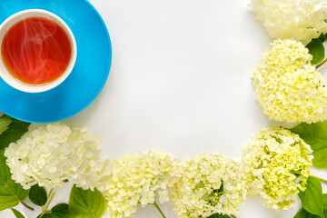Сup of hot tea with bouquet of hydrangea on white background.