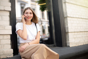 beautiful caucasian girl talking on the phone while sitting outside on the background of a black window