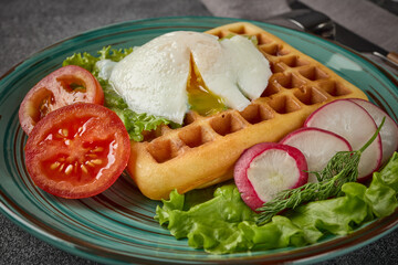 Tasty waffles with poached egg and vegetables on blue plate on grey background. Table setting