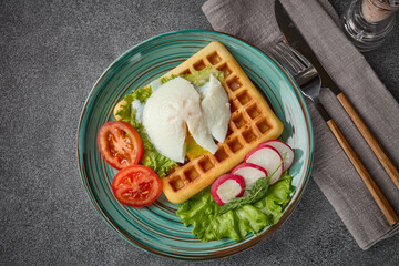 Tasty waffles with poached egg and vegetables on blue plate on grey background. Top view. Table setting