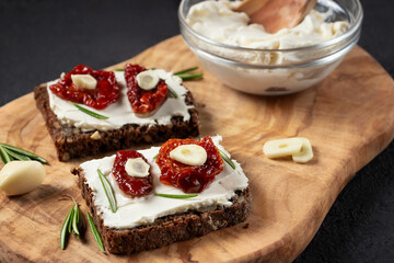 Homemade multigrain bread sandwiches with cream cheese and sun-dried tomatoes on a wooden platter. Healthy eating concept