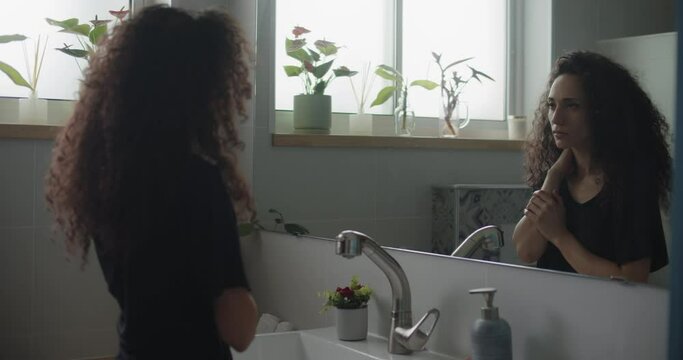 A young woman in the bathroom slowly touching her neck, feeling insecure and hurt. Slow motion, handheld, close up. 