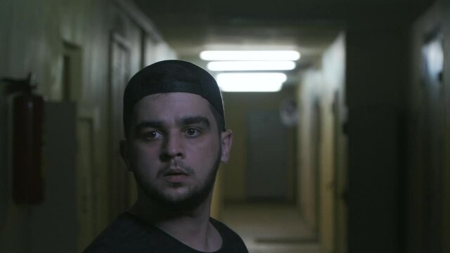 a young guy in a black cap turns around to rustle in the dark corridor