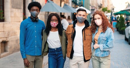 Waist up portrait view of the cheerful company of best friends wearing protective masks spending time together at the city during the covid 19 pandemic. Quarantine concept
