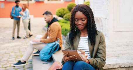 City vibes. Stylish multiracial student using her tablet computer, while enjoying at the street. Portrait of teenage girl outdoors at the summer. Urban background. Youth concept