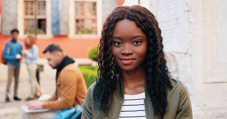 Young smiling multiracial woman wearing casual clothes using tablet computer outdoors in the street while sitting near the wall and sending messages. Slow mo, steadicam