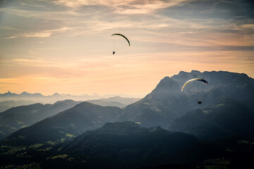 Mesmerizing view of two paragliders flying over the Austrian alps during sunset