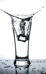 Ice in glass of water with splash on white background