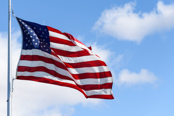 American flag flying in a breeze against a sunny blue sky with light white clouds
