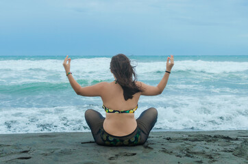 Fototapeta na wymiar Young woman from back meditating sitting on the seashore.