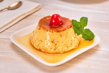 flan napolitano (mexican dessert) garnished with a cherry and a mint leaf on a white plate on a marble surface. copy space for advertising. elegant concept.