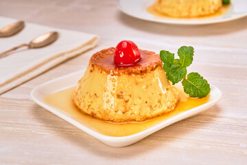 Neapolitan caramel pudding decorated with a cherry and a mint leaf on a white plate on a marble...