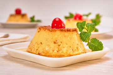 neapolitan flan with caramel decorated with a cherry and a mint leaf on a white plate on a marble surface. copy space for advertising. fancy concept. close up view
