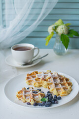 Waffles for breakfast. Belgian or Viennese waffles with berries on a white ceramic plate with a cup of aromatic coffee. 