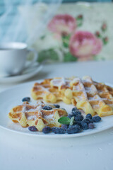 Waffles for breakfast. Belgian or Viennese waffles with berries on a white ceramic plate with a cup of aromatic coffee. 