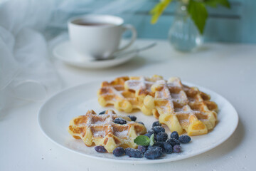 Waffles for breakfast. Belgian or Viennese waffles with berries on a white ceramic plate with a cup of aromatic coffee. 