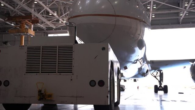 Commercial aircraft in a hangar hooked up to a push back tug.
