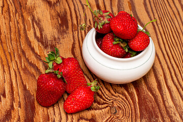 ripe juicy red strawberries in a cup and on a wooden table