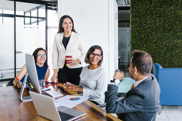 Group of Hispanic business people with transgender woman in wheelchair smiling in business meeting...