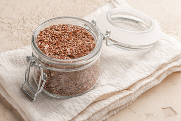 Flax seed in glass jar and napkin on beige stone background. Close-up.