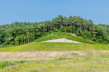 Grass covered field with new section of wall under tree lined hill. © aminkorea