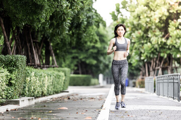 Picture of young asian women jogging in a park. She is wearing sport bra and legging. The park has concrete floor and green leaves.