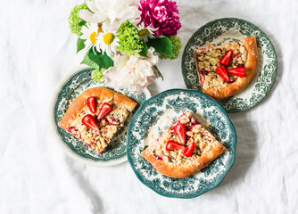 Pieces of yeast dough strawberry rhubarb sweet pie with crumbs on a light background, top view