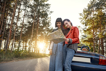 Two women trying to find the way on map near cabriolet