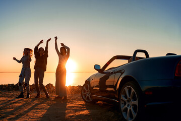 Cheerful young three women are dancing near cabriolet